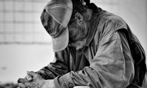 Photo en noir et blanc d’un sans-abri qui courbe le dos et baisse la tête.