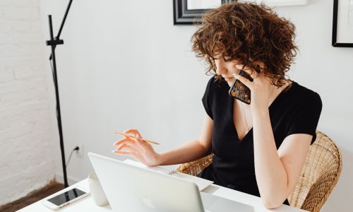 Jeune femme au téléphone devant son ordinateur et son carnet de notes.