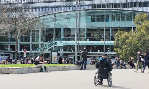 Une personne en fauteuil roulant devant la Gare Montparnasse.