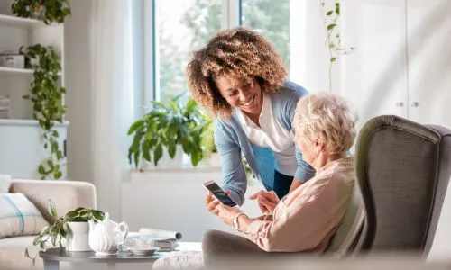 Jeune femme montre une photo à une senior en fauteuil roulant sur ton smartphone