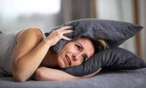 Une femme se bouche les oreilles avec un oreiller