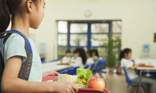 Une élève tient son plateau cherchant à s’installer à la cantine.