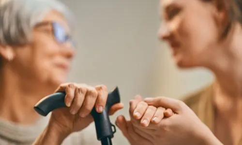 Une aidante tient la main d&rsquo;une personne qui tient une canne dans son autre main
