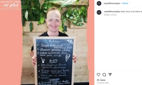 Un employé du restaurant présente le menu du jour sur une ardoise.