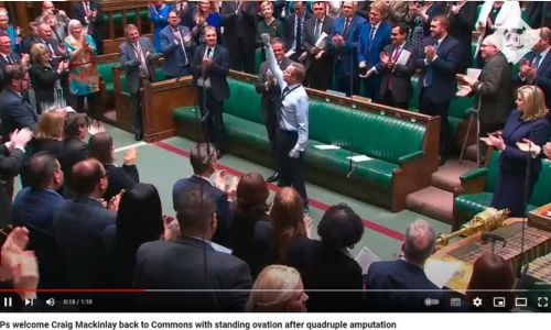 Craig levant sa prothèse de poing devant l’assemblée debout