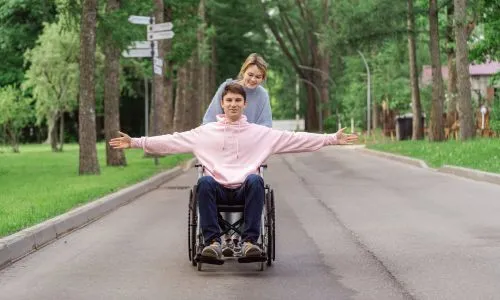 Un homme en fauteuil roulant lève les bras, heureux, poussé par sa femme.