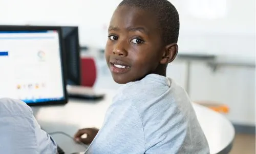 Un enfant noir sur l’ordinateur, à côté d’un autre élève, regarde l’objectif.