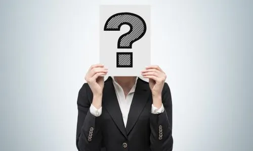 Une femme tient une pancarte avec un point d’interrogation devant son visage.