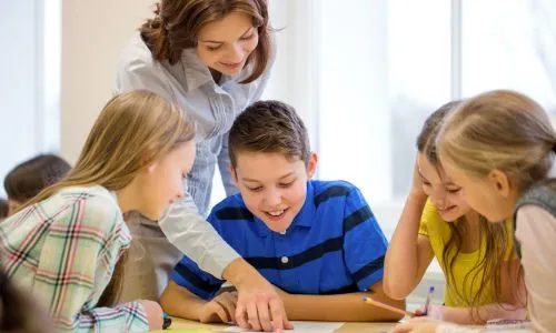 Une prof aide un élève, entouré de camarades filles, en classe.