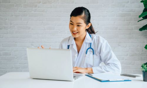 Une jeune médecin, souriante, sur son ordinateur.