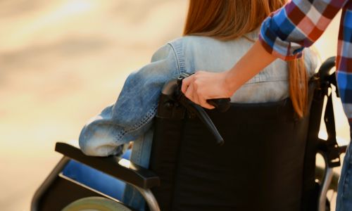 Une jeune fille en fauteuil roulant poussée par un jeune homme.