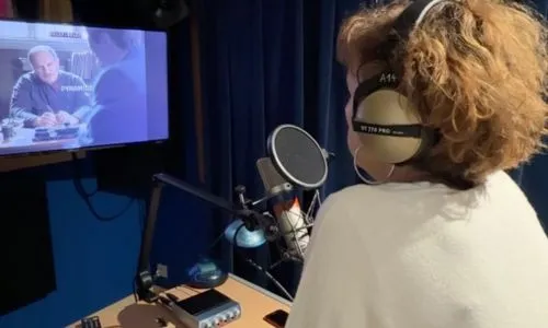 Une comédienne avec un casque sur les oreilles assise dans un studio.