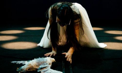 Comédienne de la troupe, sur scène, accroupie auprès du cadavre d’une mouette.