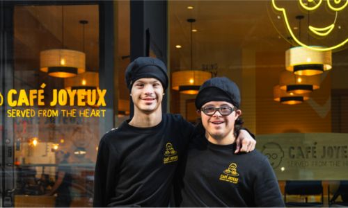 Deux équipiers du Café Joyeux sourient devant le nouveau restaurant à New York.