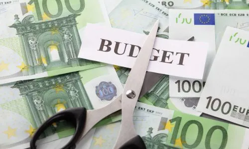 Des ciseaux coupent le mot « budget », posé sur des billets de 100 euros.