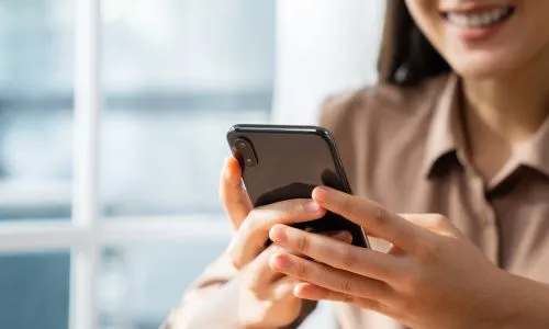 Une femme sourit en regardant son téléphone.
