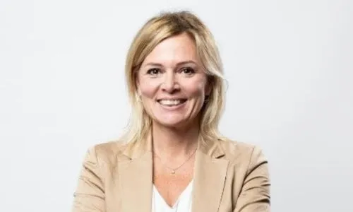 Portrait de Caroline Dekerle, femme blonde souriante vêtue d’une veste beige.