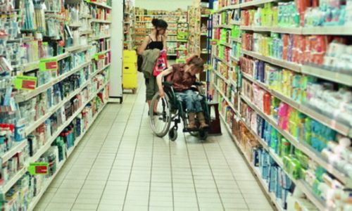 Jeune femme en fauteuil dans les allées d'un supermarché.
