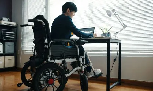 Une personne d&rsquo;origine asiatique en fauteuil roulant &eacute;crit sur son ordinateur.