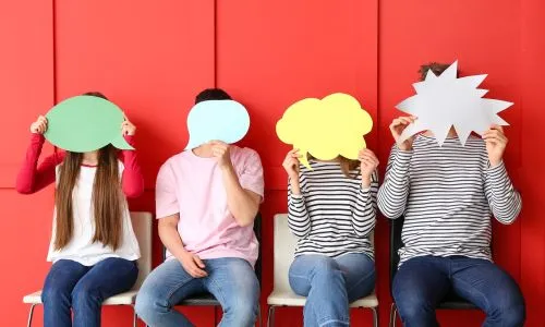4 jeunes assis sur un banc cachent leur visage avec des pancartes.