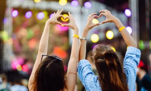 Deux jeunes femmes font des cœurs avec leurs mains à un concert en plein air.