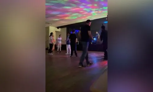 Personnes qui dansent devant un DJ sous des lumières colorées.