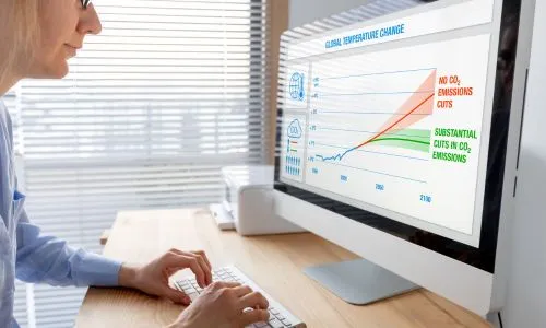 Une femme face à son ordi qui présente un graphique de l’empreinte carbone