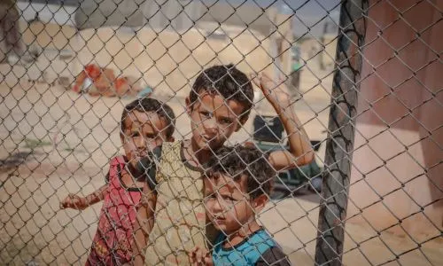 3 enfants derrière un grillage, l’air triste.