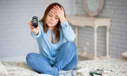 Une femme assise sur son lit, se tient la tête, en montrant son taux de glycémie
