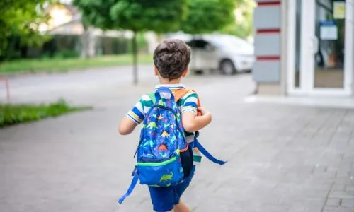 un enfant qui marche de dos avec un cartable sur le dos