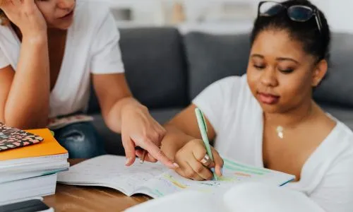 Une femme aide une &eacute;l&egrave;ve en train d&rsquo;&eacute;crire sur son cahier.