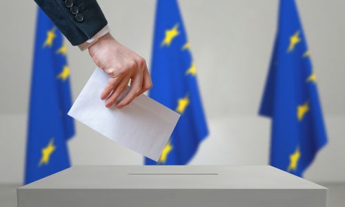 Main glissant un bulletin dans l’urne sur fond de drapeaux européens.