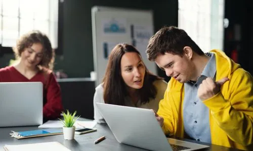 Une personne avec trisomie au bureau à côté d’une femme.