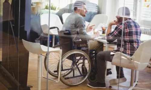 Un homme en fauteuil roulant et un valide discutent dans 1 salle de conférence.