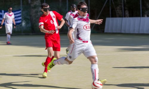 Quatre joueurs de cécifoot, avec des bandeaux sur les yeux, sur un terrain.