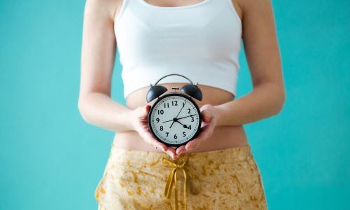 Une femme tenant une horloge devant son ventre.