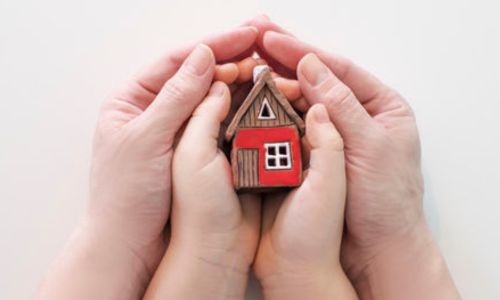 Mains d’homme enserrant des mains d’enfant tenant une maison en bois.