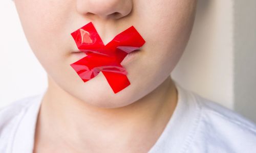 La bouche d’un enfant bâillonnée à l’aide d’une croix rouge.