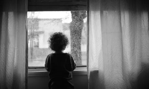 Photo en noir et blanc d&rsquo;un enfant qui regarde &agrave; travers la fen&ecirc;tre (pluie).