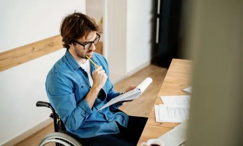 Un homme en fauteuil roulant tient un carnet de notes dans ses mains.