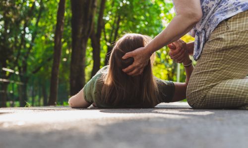 Une femme allongée à terre, de dos, secourue par une autre femme.