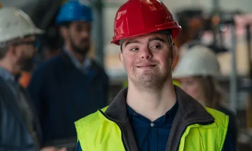Un jeune homme avec trisomie au travail, avec un casque de chantier.