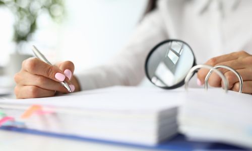 Une femme observe un rapport avec une loupe et fait des annotations.