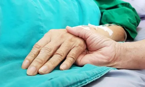 Zoom sur deux mains qui se tiennent, sur un lit d’hôpital.
