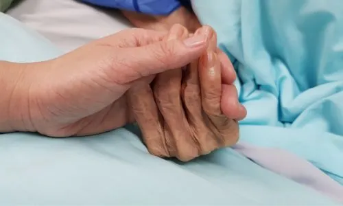 Une main &acirc;g&eacute;e tenue par un aidant ou soignant.