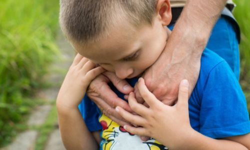 Jeune enfant triste regardant le sol entouré de bras d’adulte