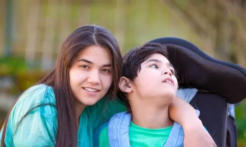 Une adolescente pose avec son fr&egrave;re en fauteuil roulant &agrave; l&rsquo;ext&eacute;rieur.