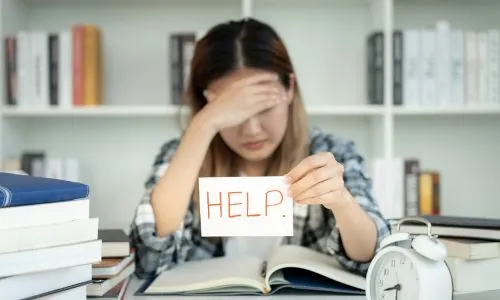 Une élève la tête baissée montre une pancarte « Help ».