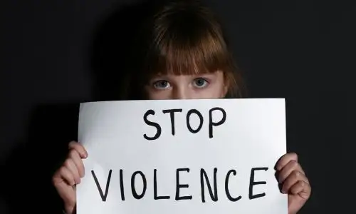 Petite fille maltrait&eacute;e avec une pancarte stop &agrave; la violence pr&egrave;s d'un mur noir