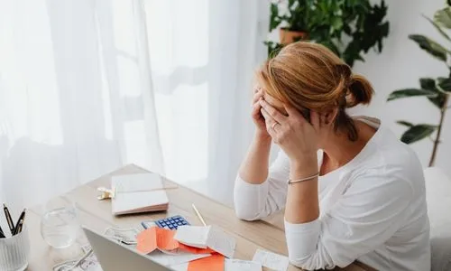 Une femme qui se tient la t&ecirc;te devant plein de factures.